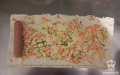 Выложите начинку равномерным слоем на лист лаваша. На край лаваша выложите сосиску и плотно сверните в рулет. Так же поступите и с оставшимися ингредиентами.