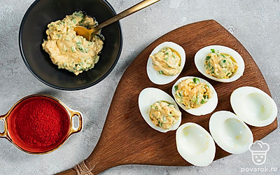 Приготовьте фаршированные яйца. Желтки разомните вилкой. Смешайте в миске желтки, нарезанный средними кусочками зеленый лук, майонез, горчицу, посолите и поперчите по вкусу, добавьте лимонного сока. Перемешайте и выложите в каждую половинку белков начинку. Затем посыпьте паприкой.