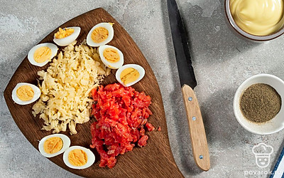 Порежьте ингредиенты для фаршированных яиц. Лосося порежьте мелкими кубиками примерно 0,2х0,2 см. Яйца разделите пополам и извлеките из каждого желток. Сыр измельчите на терке.