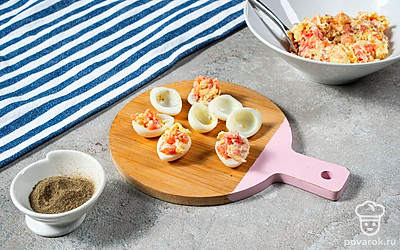 Смешайте начинку и заполните яйца. В емкости смешайте растертые желтки, лосось, сыр, майонез и молотый перец. Половинки яиц заполните начинкой.