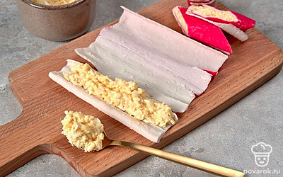 Нафаршируйте палочки. Палочку разверните белой стороной вверх, распределите по поверхности яично-рисовую начинку, сверните трубочкой, разрежьте ее на 2-3 части. Аналогично поступите с оставшимися крабовыми палочками.