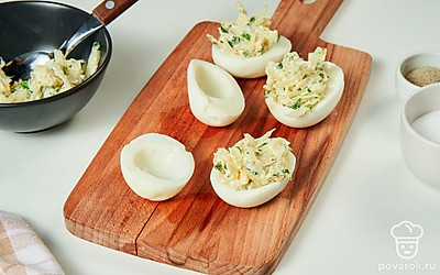 Приготовьте фаршированные яйца. Смешайте в отдельной миске сыр, чеснок и кинзу. Добавьте к ним желток, майонез, посолите и поперчите по вкусу. Тщательно перемешайте. В половинки белков выложите примерно с чайную ложку начинки.