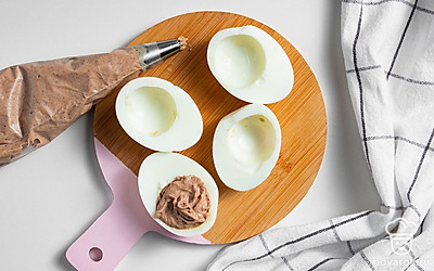 Приготовьте фаршированные яйца. Начинку переложите в кондитерский мешок. Полые белки яиц выложите на тарелку и заполните печеночной смесью.