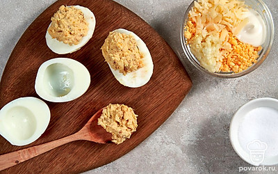 Сделайте начинку. Сыр натрите на мелкой терке и смешайте с желтками, оставив немного для украшения. Чеснок пропустите через пресс и добавьте к смеси. Ингредиенты смажьте майонезом, посолите по вкусу и перемешайте до однородности. Готовую начинку разложите по половинкам белков.