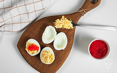 Приготовьте фаршированные яйца. Соедините сырную массу с чесноком и майонезом, взбейте ее. Полые белки нафаршируйте подготовленной начинкой и сверху выложите икру.