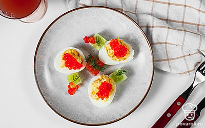 Готовые яйца, фаршированные икрой, положите на прямоугольную черную тарелку. Украсьте каждую половинку яйца одной оливкой и листочком базилика.