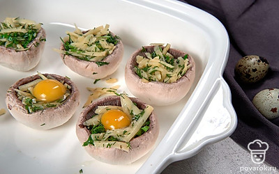 Запеките грибы. На противне уложите шампиньоны шляпками вниз, распределите начинку, оставив место для яйца. Затем разбейте по перепелиному яйцу и отправьте в горячую духовку на 15 минут.