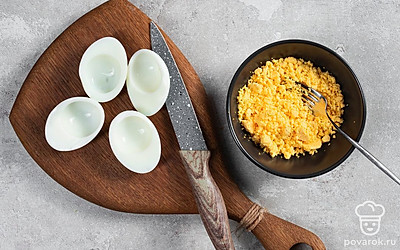 Подготовьте основу. Яйца очистите от скорлупы и разрежьте на половинки, выложив их на блюдо. Извлеките желтки и разомните их вилкой в отдельной миске.