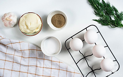 Куриные яйца сварите вкрутую, после чего остудите в холодной воде и очистите от скорлупы. Укроп и огурец для подачи тщательно промойте, просушите. Зелень измельчите. Зубчик чеснока очистите от шелухи и измельчите в прессе.