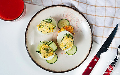 Аппетитную закуску в виде фаршированных яиц подавайте к столу в качестве дополнения к основному блюду. А чтобы закуска смотрелась интереснее, украсьте ее огурцом. Нарежьте овощ вдоль тонкими пластинами, после чего воткните их в начинку. Подавайте блюдо на прямоугольной тарелке или на дощечке.