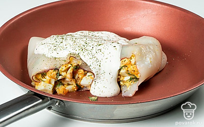 Приготовьте блюдо. На сковороду налейте растительное масло и поместите ее на средний огонь. Пока масло разогревается, нафаршируйте кальмары, плотно уложив начинку в тушку морепродукта. Кальмары положите на сковороду, добавьте сметану и воду. Дождитесь, когда соус закипит, после чего переверните фаршированные кальмары и потушите их еще пару минут.