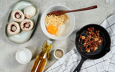 Подготовьте начинку. Натрите сыр на мелкой терке. Разбейте яйцо в миску, добавьте сыр и панировочные сухари, посолите и поперчите. Отделите шляпки от ножек у грибов. Чеснок выдавите с помощью пресса. Мелко нарежьте ножки шампиньонов и обжарьте с чесноком на оливковом масле 5 минут. Выложите в сырную начинку, перемешайте.