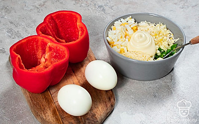 Начните приготовление. Одно куриное яйцо измельчите. Плавленый сыр натрите на средней терке. В отдельную миску выложите майонез. Чеснок измельчите, зеленый лук мелко порубите, после чего переложите ингредиенты к майонезу. Туда же добавьте сыр и яйцо, хорошо перемешайте. Готовой смесью промажьте внутренние стенки перцев, оставляя место для целого яйца.