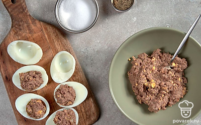 Приготовьте яйца, фаршированные куриной печенью. Половинки яичных белков ополосните водой, просушите. С помощью маленькой ложечки выложите начинку в свободную полость белка. Сформируйте аккуратную горку. Охладите закуску.