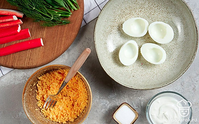 Подготовьте основу. Яйца очистите от скорлупы и разрежьте пополам. Желток достаньте, переложите его в отдельную миску и разомните. Части белков разложите на тарелке.