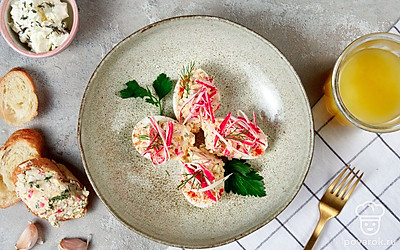 Отложенную крабовую палочку нарежьте соломкой и украсьте ей каждую половинку. Вместе с ней в центр воткните по листику петрушки для красоты и аромата.