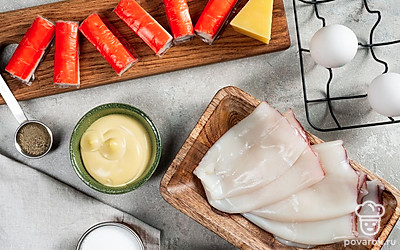 Достаньте кальмары из морозилки, чтобы они разморозились. Крабовые палочки нарежьте кубиками. Яйца сварите вкрутую, остудите в холодной воде, почистите и нарежьте кубиками. Сыр натрите на терке. Немного тертого сыра отложите для подачи. Включите духовку на 180 градусов.