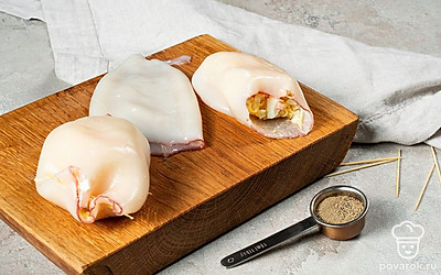 Приготовьте фаршированные кальмары. В каждую тушку кальмара выложите начинку на ¾ полости. Скрепите каждое отверстие зубочисткой. Выложите нафаршированные кальмары на противень и поставьте запекаться в духовку на 15 минут.