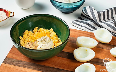 Приготовьте начинку. Вареные яйца разрежьте на две части, желток извлеките и переложите в отдельную емкость. Туда же добавьте майонез, сметану и горчицу. Желток тщательно разомните, после чего перемешайте ингредиенты до однородной массы. Готовую смесь приправьте солью и перцем по вкусу, а затем накройте ее пищевой пленкой и уберите в холодильник.