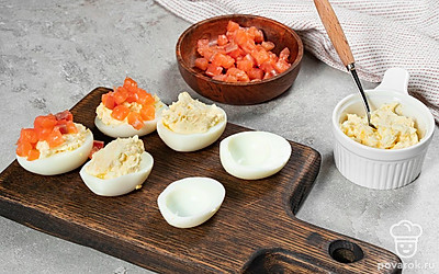 Приготовьте фаршированные яйца. В отдельной миске смешайте майонез, творожный сыр и желтки. Выложите начинку в половинки белков. Затем уложите сверху кусочки семги.