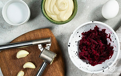 Подготовьте свеклу. Овощ отварите до готового состояния в течении 20-25 минут. Остудите. Снимите кожуру, натрите плоды на средней терке. Пропустите через пресс чеснок. Соедините со свеклой.