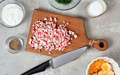 Займитесь нарезкой продуктов. Яйца разрежьте вдоль на половинки. Желтки переложите в глубокую миску, разомните. Замороженные крабовые палочки пропустите через терку со средними зубчиками. Зелень измельчите.