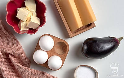 Яйца сварите вкрутую, остудите и очистите. Нарежьте их кубиками среднего размера. Сыр натрите на терке с крупными ячейками. Сливочное масло достаньте заранее, что оно стало мягким. Баклажан вымойте, обсушите бумажными полотенцами. Приготовьте миску и форму для запекания.