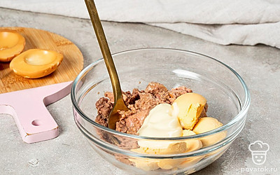 Приготовьте начинку. Печень трески переложите в глубокую миску, лишнюю жидкость слейте. Туда же добавьте яичные желтки и майонез. Тщательно перемешайте ингредиенты.