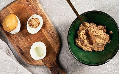 Приготовьте закуску. Аккуратно наполните яичные белки готовой начинкой до краев и поставьте на блюдо срезом вниз. Сверху накройте яйца приготовленными заранее «шляпками», которые за счет варки в черном чае окрасились в коричневый цвет.