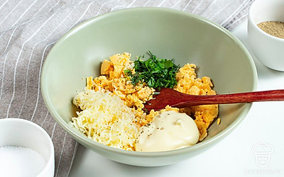 Подготовьте яйца и начинку. Очищенные от скорлупы яйца разделите на 2 части и извлеките желтки. Все желтки переложите в отдельное блюдце, разомните вилкой и добавьте к ним нарезанную зелень и тертый сыр. Следом положите в начинку майонез, посолите, поперчите и все хорошо перемешайте.