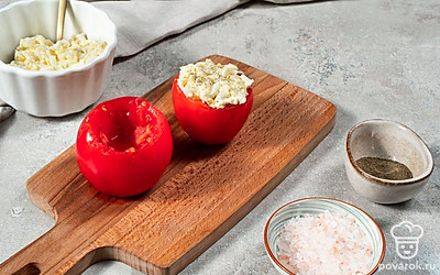 Приготовьте фаршированные помидоры с яйцом и чесноком. Разрежьте томаты на две половины. Ложкой удалите мякоть. Выложите в помидоры начинку с горкой. Охладите в течение 10 минут.