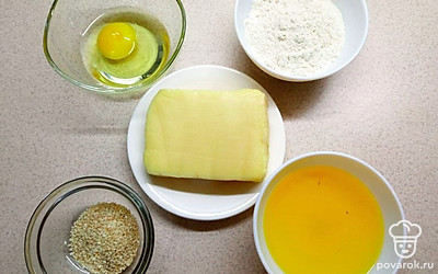 Сыр распакуйте и положите в тарелку. Яйцо разбейте в пиалу. Растительное масло, кунжут, муку распределите пропорционально по пиалам и положите на стол.