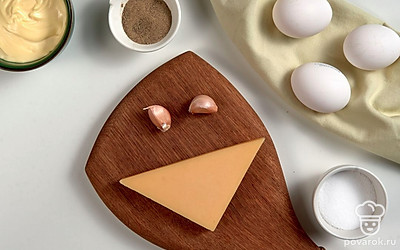 Яйца сварите вкрутую, остудите и очистите. Разрежьте их пополам, извлеките и измельчите желтки. Зелень петрушки вымойте, обсушите и мелко нарубите. Чеснок почистите, вымойте и выдавите через пресс. Сыр натрите на терке с мелкими ячейками. Четверть сыра отложите в сторону, чтобы использовать для украшения. Приготовьте сервировочное блюдо.