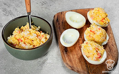 Сделайте начинку из крабовых палочек. В миске смешайте желтки, крабовые палочки, сыр, чеснок и майонез. При необходимости посолите. В порционную тарелку положите белки и аккуратно наполните их начинкой. Затем уберите на 10-15 минут в холодильник для охлаждения.