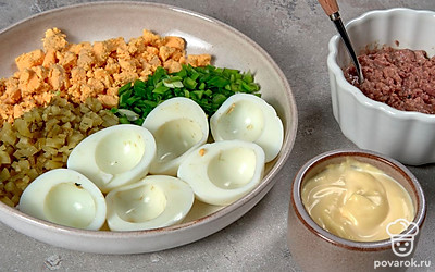 Подготовьте продукты. Печень трески разделите на маленькие кусочки, затем разомните. Мелко нашинкуйте зеленый лук. Кубиками небольшого размера нарежьте огурцы. Желтки измельчите в крошку.