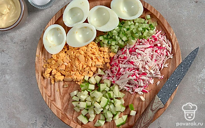 Подготовьте ингредиенты для начинки яиц. Яйца разрежьте пополам. Желтки уберите и измельчите. Мелко нашинкуйте укроп, яблоки и огурцы. Крабовые палочки натрите на средней терке.