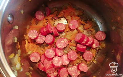 Добавить колбаски к зажарке. Обжарить вместе с луком и морковкой в течение 5 минут. 