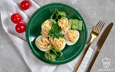 В центр сервировочной тарелки расставьте яйца, фаршированные желтком с майонезом. Верх закуски присыпьте измельченной зеленью, края тарелки оформите дольками огурца.