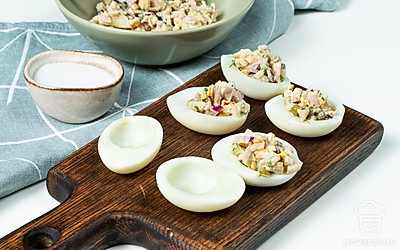 Нафаршируйте яйца. Выложите в миску желтки, кальмары, лук и укроп. Добавьте зеленый горошек, соль и майонез. Перемешайте. Начинку разложите в яичные белки.