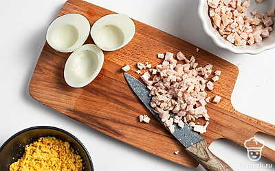 Займитесь начинкой. Яйца разрежьте на две половины, желтки уберите, измельчите в крошку. Курицу нарежьте на мелкие кусочки. Укроп накрошите. Чеснок продавите через пресс. Маслины нарежьте на кружочки.