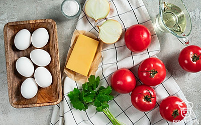 Помидоры вымойте, обсушите бумажным полотенцем. Сыр натрите на терке с мелкими ячейками. Лук очистите, помойте и нарежьте кружочками. Вымойте и порубите петрушку. Помойте яйца. Маслины порежьте колечками. Приготовьте форму для запекания.