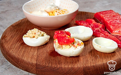 Нафаршируйте яйца. В миске желтки измельчите вилкой или блендером. Смешайте с желтками сушеные чеснок и лук, всыпьте кунжут, заправьте майонезом. Влейте лимонный сок и выложите сливочный сыр. Смесь тщательно размешайте или пюрируйте блендером. Нафаршируйте смесью куриные белки. Сверху выложите свернутые в трубочку кусочки рыбы.