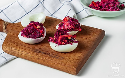 Приготовьте закуску к подаче. В глубокую емкость положите тертую свеклу, посолите. Добавьте майонез, морковь, желток, измельченную селедку, чеснок и зеленый лук. Тщательно перемешайте. В белки яиц распределите начинку, сформируйте аккуратную горку.