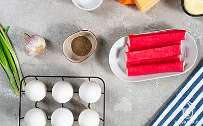 Яйца сварите вкрутую, остудите и очистите. Яйца разрежьте пополам, извлеките из них желтки. Чеснок почистите и вымойте. Крабовые палочки извлеките из упаковочной пленки. Зелень вымойте, обсушите на бумажных полотенцах. Оливки для подачи нарежьте колечками.