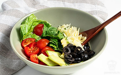 Оформите салат. Возьмите пиалку, положите в нее листья салата. Затем выложите авокадо, помидоры и маслины. Полейте заправкой. Перемешайте и сверху посыпьте сыром.