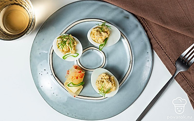 Сыр натрите на мелкой терке в отдельную тарелку, а затем аккуратно посыпьте им каждую половинку яиц. Финальный штрих — свежая зелень петрушки. Украсьте ей блюдо и подавайте к столу.