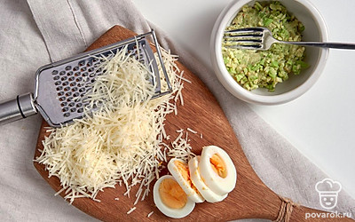 Подготовьте ингредиенты для блюда. Авокадо разделите пополам, уберите косточку, полейте соком лимона. Разомните мякоть с помощью вилки. Яйца нарежьте средними кружочками. Сыр натрите на мелкой терке.