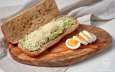 Приготовьте чиабатту с авокадо. Чиабатту разрежьте пополам вдоль. Немного обжарьте каждый кусочек хлеба на сухой сковороде. Смажьте их массой из авокадо. Сверху положите тертый сыр. Поверх выложите кружочки яиц.