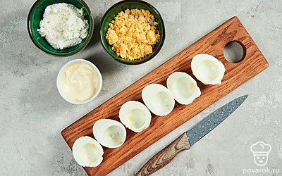 Подготовьте основу. Вареные яйца очистите от скорлупы и разрежьте пополам. Разложите половинки на блюде, желтки извлеките и тщательно разомните их вилкой в отдельной емкости.