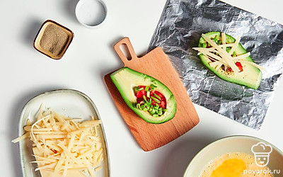 Нафаршируйте авокадо. Положите половинки авокадо на фольгу. В ямки, оставшиеся от косточки, выложите часть томатов и лук. Полейте яйцом, посолите, поперчите и посыпьте сыром. Заверните фольгу и поставьте в духовку на 10-15 минут.